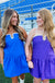 Two women in blue and purple dresses standing on grass with bleachers in the background
