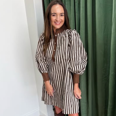 Woman wearing a black and white striped dress standing in front of a green curtain.
